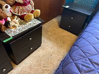 Pair of dark laminate nightstands positioned on carpet next to bed with two drawers each and round metal knobs.