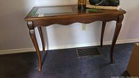 Side view of wooden sofa table showing curved legs and glass top with woven inset.