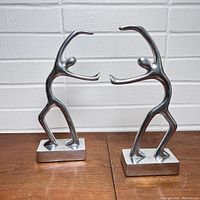 Front view of the pair of abstract metal men bookends showing the stylized figures with raised arms on rectangular bases.