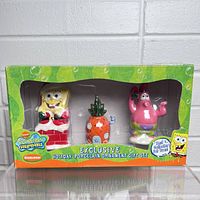 Front view of the sealed box containing SpongeBob SquarePants holiday porcelain ornament set. Shows SpongeBob in Santa outfit, pineapple house, and Patrick Star figurines clearly visible inside.