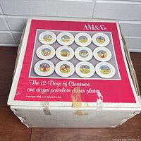 Closed original box showing AM&As branding and image of the 12 plates depicting the 12 Days of Christmas.