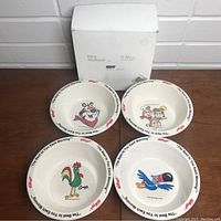Four Kelloggs cereal bowls displayed on a wooden surface with white wall background. Included original white box behind the bowls. Each bowl features different character artwork.