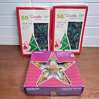 Two unopened boxes of 50 cactus-style Christmas lights each with window showing colored bulbs inside, and a boxed Noma tree top star in front