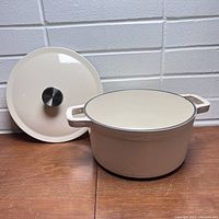 Photo of the vintage white enamel coated cast iron pot with lid on a wooden surface against a brick wall background.