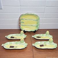 Full view of the entire vintage ceramic corn on the cob serving set showing 1 large serving dish, 4 corn trays each with salt and pepper shakers, and a pair of tongs.