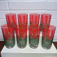Set of 8 tall clear glasses with red vertical stripes and embossed holly leaves with red berries around the lower portion.