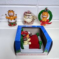 Four Garfield Christmas ornaments: drummer Garfield, Santa Claus Garfield, Garfield wreath, boxed Garfield in bed with 1988 label.