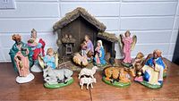 Full nativity set with stable, figures of Holy Family, Wise Men, angels, and animals displayed on wooden surface against white brick background.