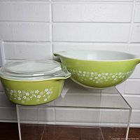 View of the vintage PYREX Spring Blossom 2.5 liter bowl alongside the 750 ml covered casserole dish with lid, clearly showing green color and white floral pattern.