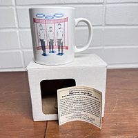 White ceramic mug with Star Trek "Beam Me Up" transporter graphic in red and blue colors displayed on the side. The mug is shown on top of a white box with a care instructions leaflet visible.