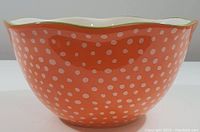 Front view of the large orange mixing bowl with white polka dots and scalloped green rim
