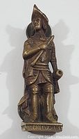 Front view of brass door knocker shaped as a soldier holding a horn and sword.