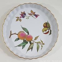 Top-down photo of the oval quiche dish showing peach, pear, and blackberry fruit designs with scalloped gold-edged rim