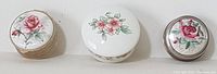Top view showing three vintage pill boxes with floral porcelain tops sitting on a white surface.