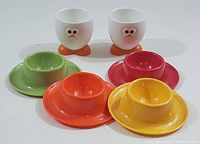 Photo showing all 6 egg cups arranged with four colorful plastic/melamine egg cups in front and two white cartoon face egg cups behind.