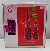 Two boxed collapsible tinsel Christmas trees shown on front packaging. Box is white with pink decorative patterns and a clear window showing tree material.