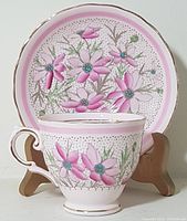 Front view of porcelain cup and saucer featuring pink floral designs and gold rims.