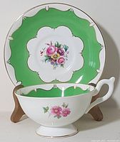 Front view of teacup placed in front of saucer clearly showing floral patterns and green border with gold trim.