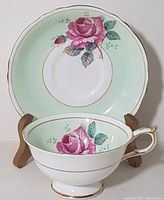 Front view of Paragon teacup and matching saucer showing detailed pink rose and mint green design with gold trim.