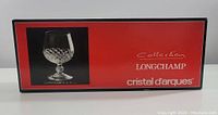 Box of Cristal d'Arques Longchamp brandy glass showing product image, brand and collection name on red and black background.
