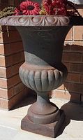 Full view of the large cast iron planter showing its shape, design, and weathered condition with floral arrangement on top (not included).