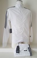 Front and side view of white full zip jacket with black stripes on shoulders and sleeves, displayed on a mannequin.