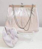 Front view of the vintage shiny silver evening bag with metal frame and silver chain strap alongside the smooth satin-like silver change purse.