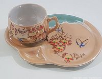 Photo showing cup and divided snack plate featuring hand-painted floral branches and colorful birds in lustreware finish.