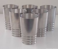 Six vintage pewter cups arranged in a row showing design and quantity.