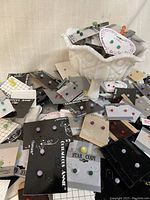 Photo showing a large quantity of carded vintage stud earrings in various colors and brands, placed in and around a white footed milk glass bowl.