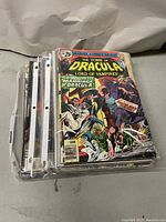 Photo of a stack of assorted Marvel, DC, and independent comic books in plastic sleeves showing The Tomb of Dracula comic on top with colorful cover art.