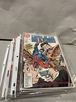 Stack of assorted comic books in plastic sleeves, front comic is DC Comics 'Powers of the Atom' with colorful superhero action cover.
