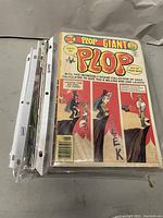 Photo showing assorted comic books stacked and some in protective sleeves, with one visible comic book titled 'Plop Giant' on top.