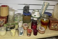 Assorted new home fragrance items including various jar candles, pillar candle, reed diffuser sticks and ceramic holder, wax melts, and boxed candle sets.