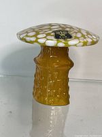 Front view of yellow and white spotted hand blown glass mushroom with original label on cap.