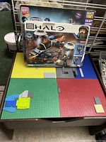 Reversible Lego-compatible playboard activity table with Mega Bloks Halo Galactic Gateway Station block set box on top and multicolor baseplates on surface.