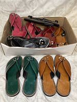Box of various colored Tunisian genuine leather sandals including black, red, green, brown, and tan pairs, arranged with some pairs inside a box and some displayed in front.