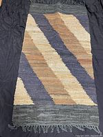 Full view of the rectangular handwoven leather chindi area rug with diagonal stripes in tan, beige, and navy blue colors on a dark background.