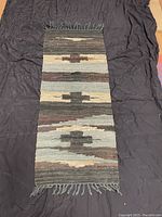 Full view of the 17 by 44 inch handwoven leather chindi rug showing striped geometric pattern and fringed ends on black backdrop.