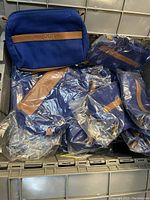 Lot of 20 vintage Joop blue canvas cosmetic travel bags, wrapped in plastic, stacked together.