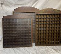 Three vintage wooden thimble cabinets with many square compartments for storing thimbles or small items. One cabinet has a painted top with bird and flower designs. Cabinets show wear from use.
