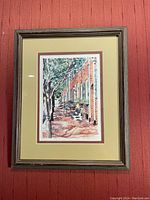 Framed watercolor painting showing a tree-lined brick walkway with benches, signed by Lisa Madenspacher.