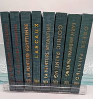 Eight vintage hardcover Skira art books standing upright side by side, showing spines with gold lettering on dark green cloth covers, next to a ruler for scale.