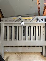 Disassembled gray painted pine bed panels and rail components stacked on floor