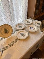 Six NIKKO octagonal Christmas tree dinner plates displayed on a tablecloth with the Christmas tablecloth partly visible.