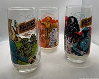 Three Star Wars collector glasses with colorful graphics from Empire Strikes Back depicting characters including Yoda, C-3PO, R2-D2, Darth Vader, and Boba Fett.