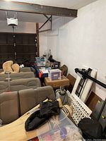 View of air hockey table stored in cluttered garage with surrounding items and furniture.