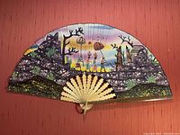 Full view of large hand-made batik fan with colorful scenic design and wooden ribs.
