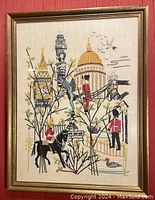 Front view of London crewel embroidery framed with glass showing city landmarks and guards with horse.