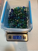 Plastic container holding about 6.26 lbs of mixed-color glass marbles on a digital scale.
